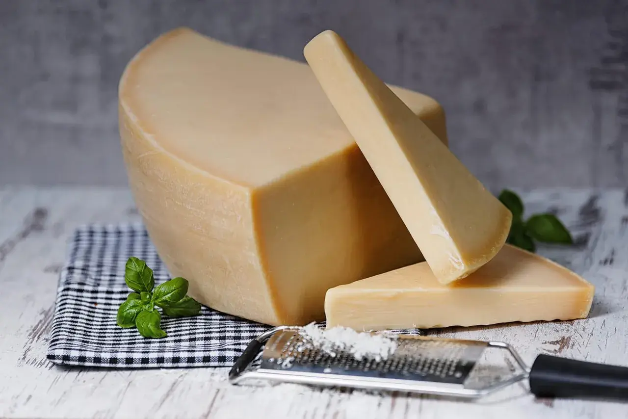 Twardy, żółty ser, przypominający parmezan- polski odpowiednik, leży obok tarki z wiórkami.