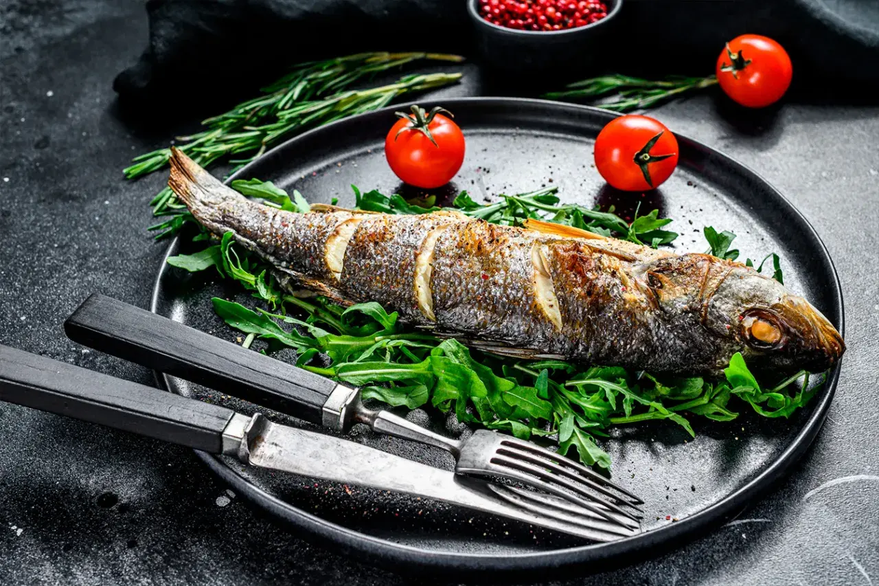Un bar au four, doré et savoureux, servi sur un lit de roquette avec des tomates cerises et des herbes. Un plat simple et élégant.