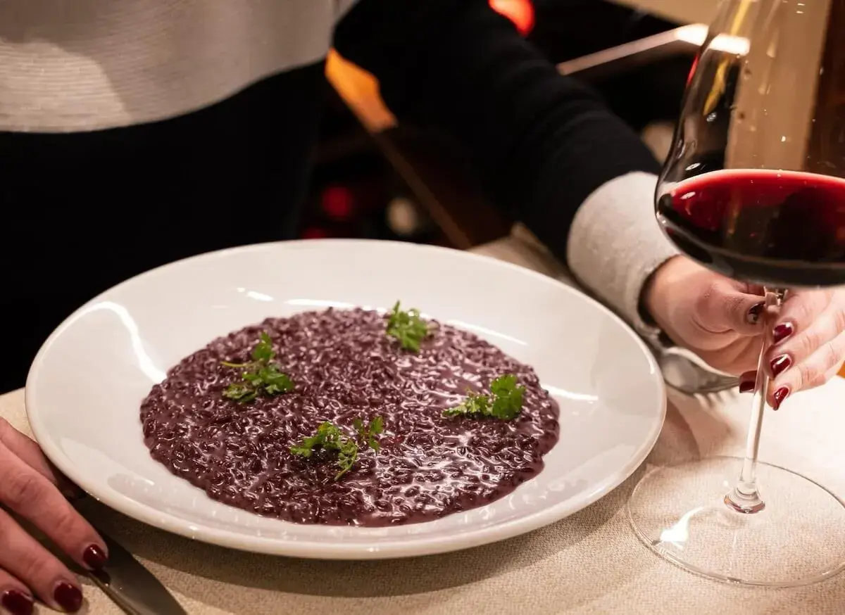Risotto viola con prezzemolo, accompagnato da un calice di vino rosso. Perfetto per scoprire i migliori amarone abbinamenti.