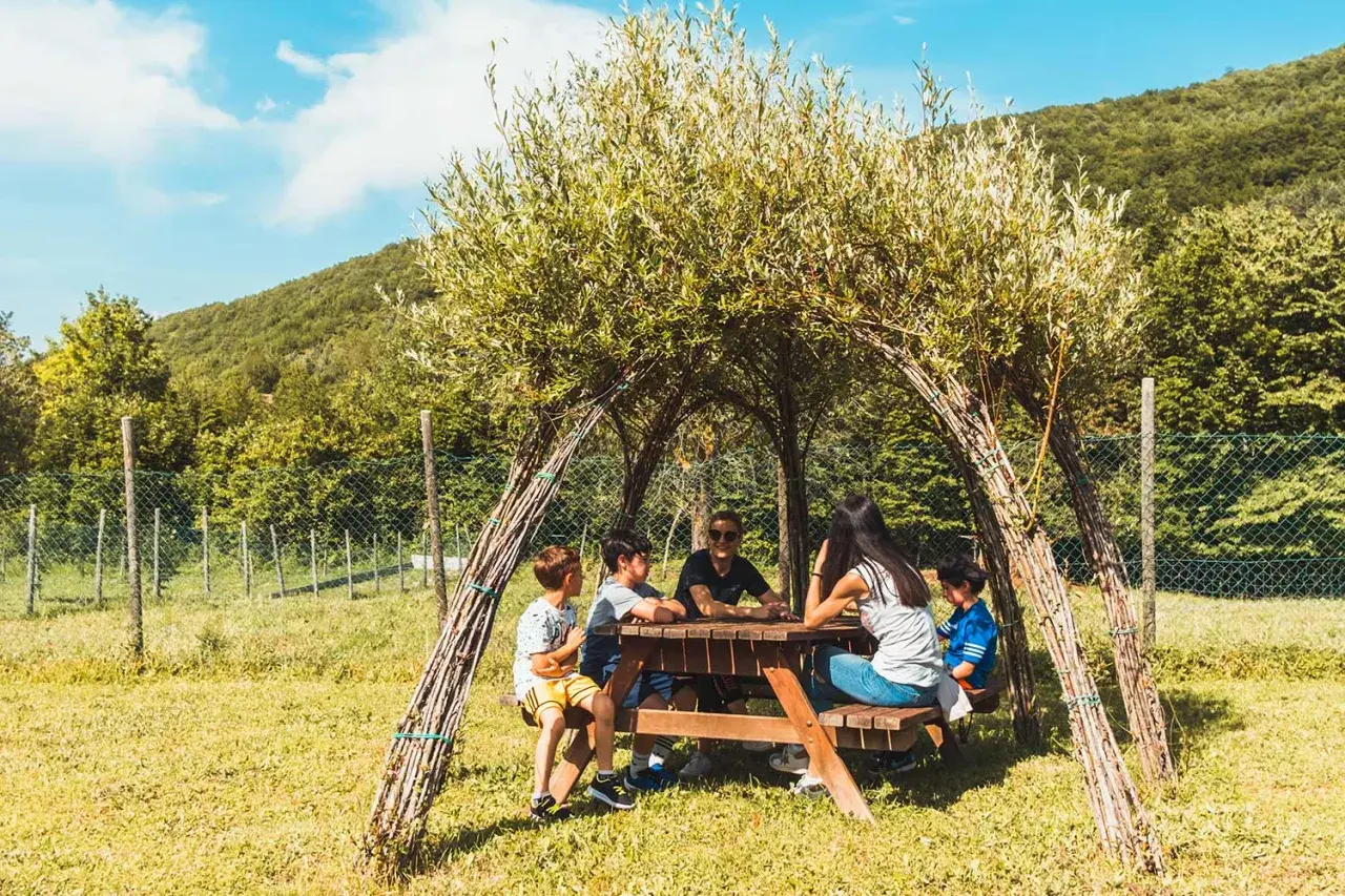 Bambini riuniti attorno a un tavolo da picnic sotto una tettoia naturale nel bosco dei folletti Urbania.