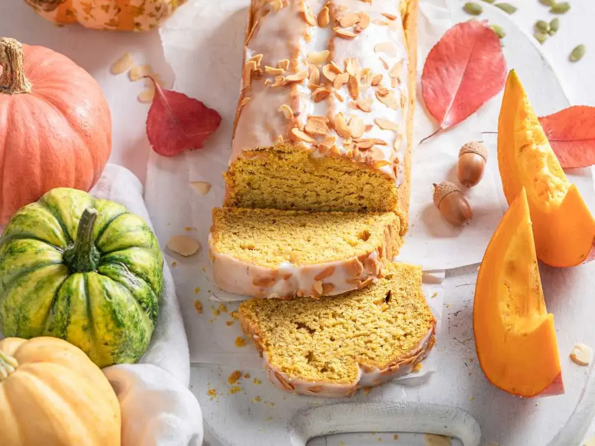 Bizcocho de calabaza Thermomix cubierto de glaseado y almendras. Rodeado de calabazas, hojas de otoño y bellotas.
