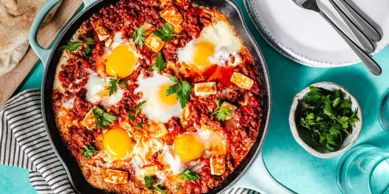 Chakchouka sans poivron : œufs pochés dans une sauce tomate épicée, parsemée de fromage halloumi grillé et de persil frais.
