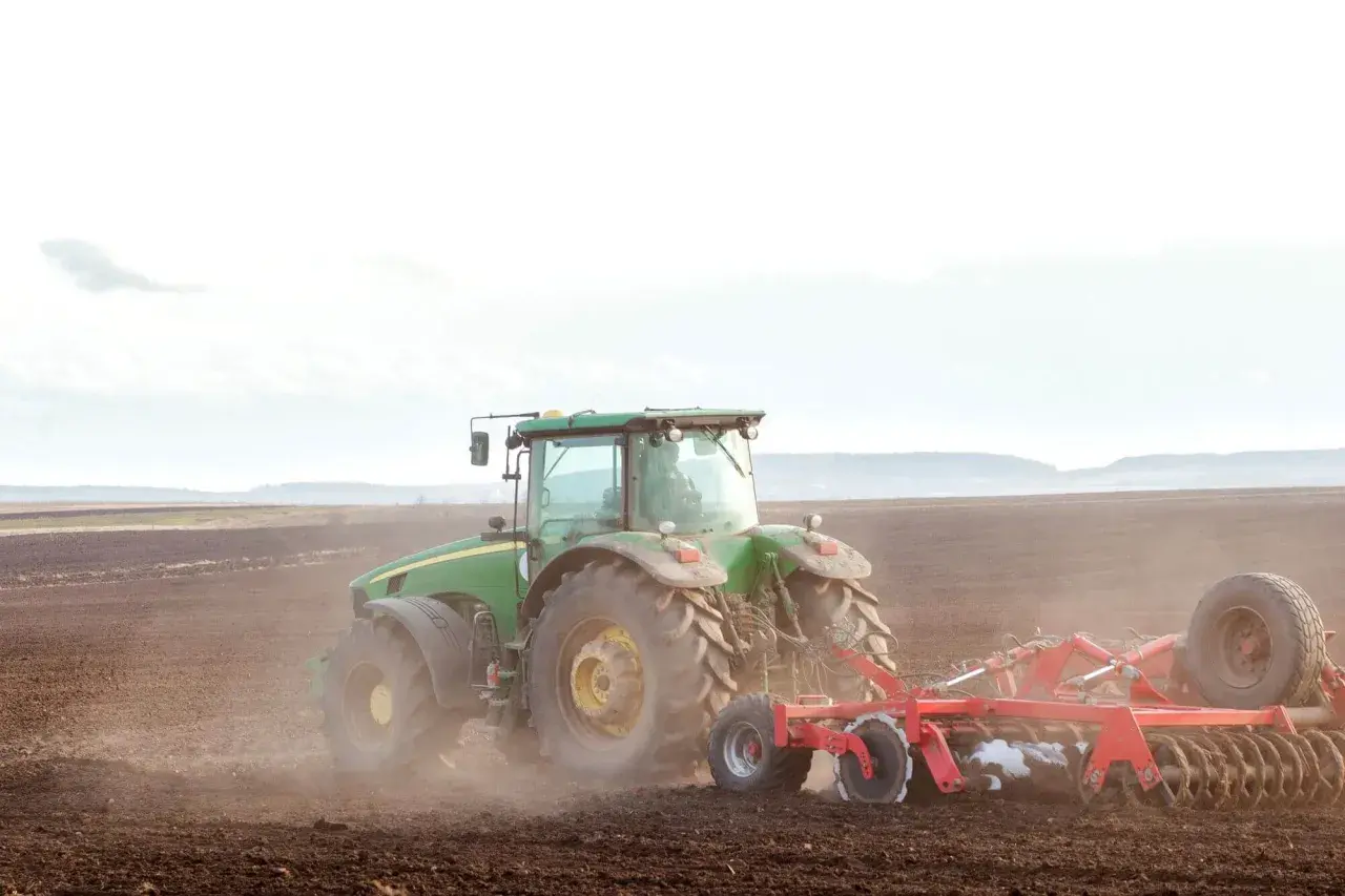 Zielony traktor orze pole. To obraz przyszłości, gdzie przekazanie gospodarstwa rolnego idzie w parze z opieką nad rodzicami, zapewniając stabilność i ciągłość.