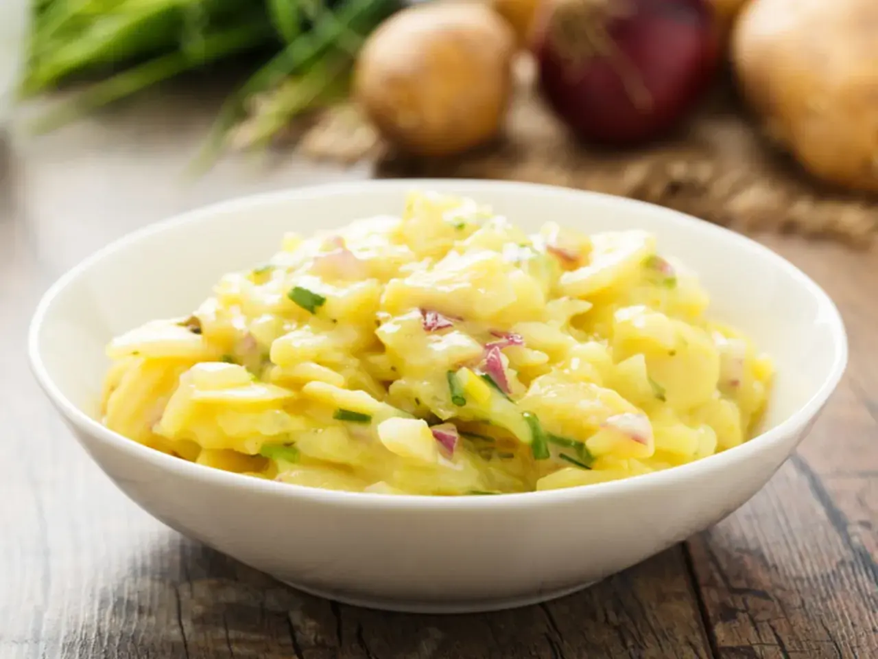 Omas Kartoffelsalat in einer Schüssel, mit Zwiebeln und Schnittlauch, auf einem Holztisch.