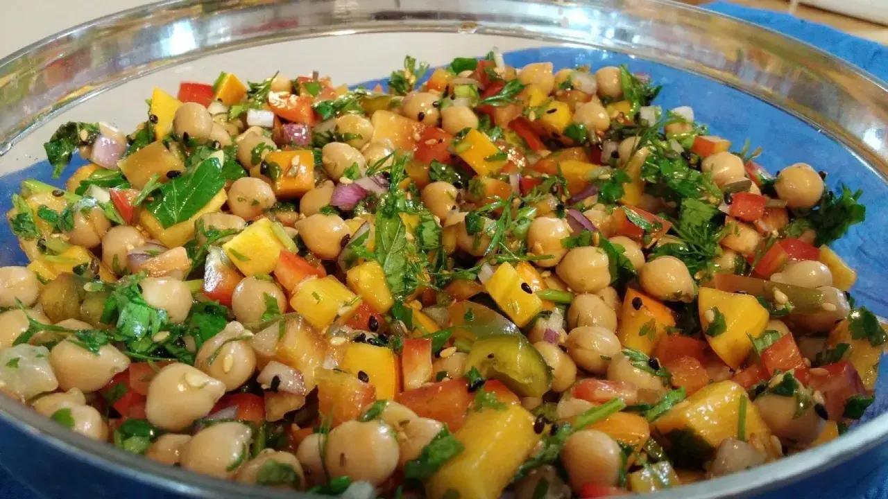 Ensalada de legumbres vibrante con garbanzos, pimientos de colores, cebolla morada y cilantro fresco, todo mezclado en un bol de vidrio.