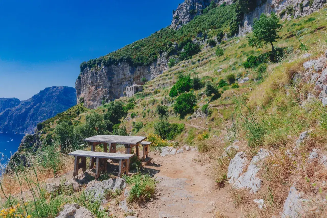 Un tavolo da picnic in legno attende i viaggiatori sul Sentiero degli Dei, con vista mozzafiato sul mare e sulle montagne.
