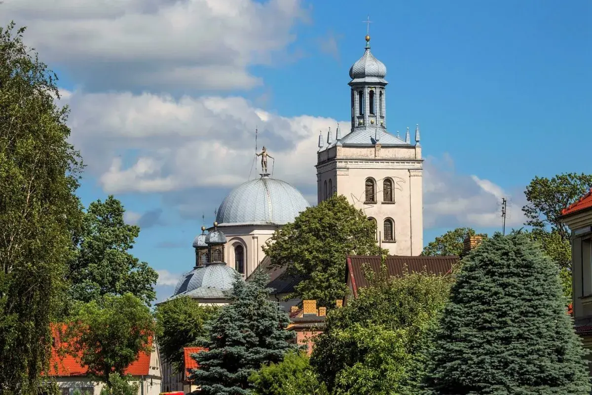 Majestatyczna fara w Grodzisku Wlkp. z kopułą i wieżą, otoczona zielenią drzew.