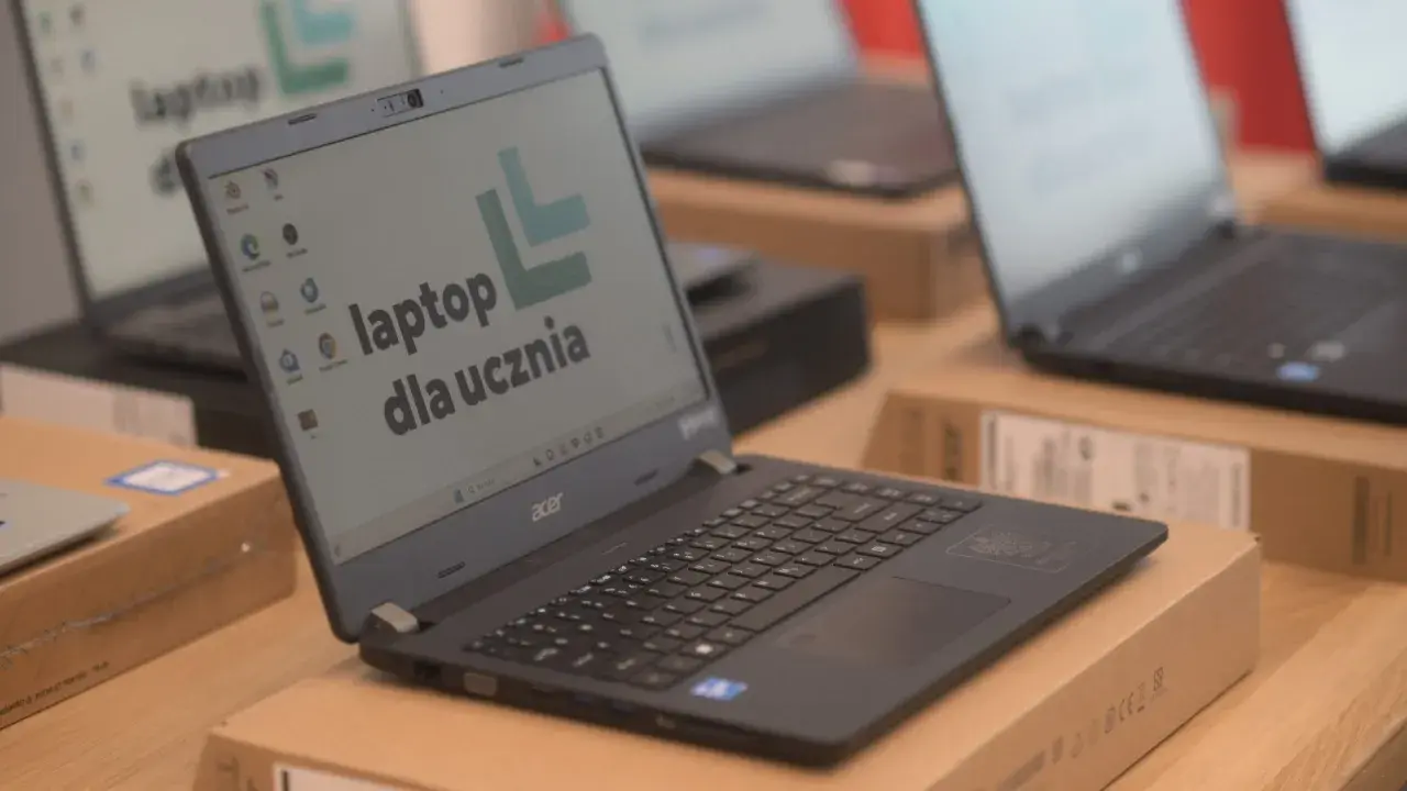 Laptop Acer z napisem "laptop dla ucznia" na ekranie, otoczony innymi laptopami i pudełkami.