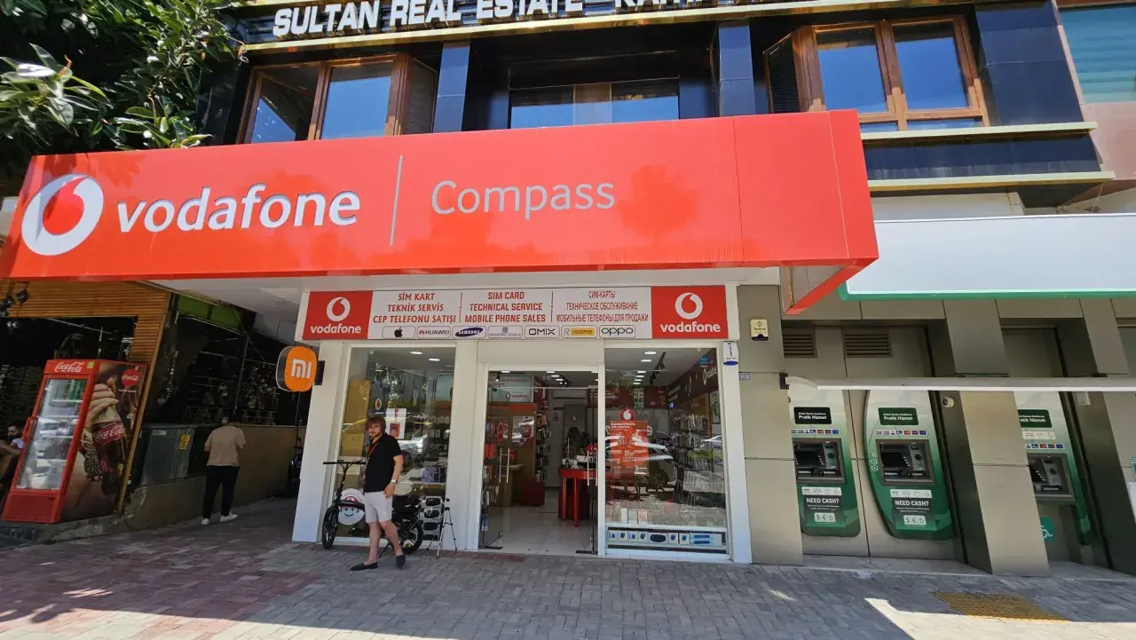 Sklep Vodafone z szyldem "Compass", bankomaty i lodówka Coca-Cola.
