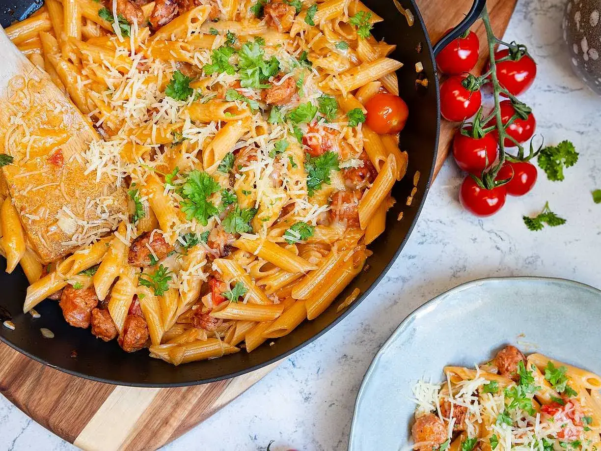 En stor panna med krämig pasta med chorizo, toppad med riven ost och färsk persilja. Bredvid syns en tallrik med samma läckra pasta.