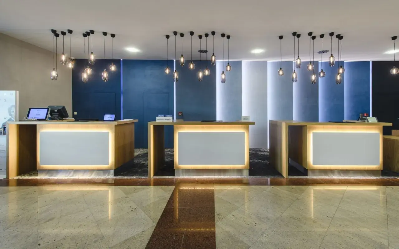 Recepcja hotelowa z trzema ladami, nowoczesnymi lampami i podświetlanymi panelami.