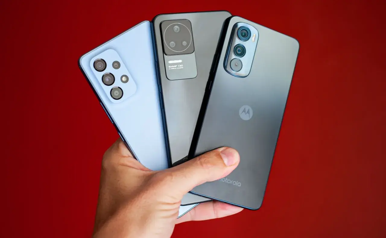 Dłoń trzyma trzy smartfony: jasnoniebieski, szary i ciemnoszary z logo Motorola. Kraj pochodzenia tej marki to USA.