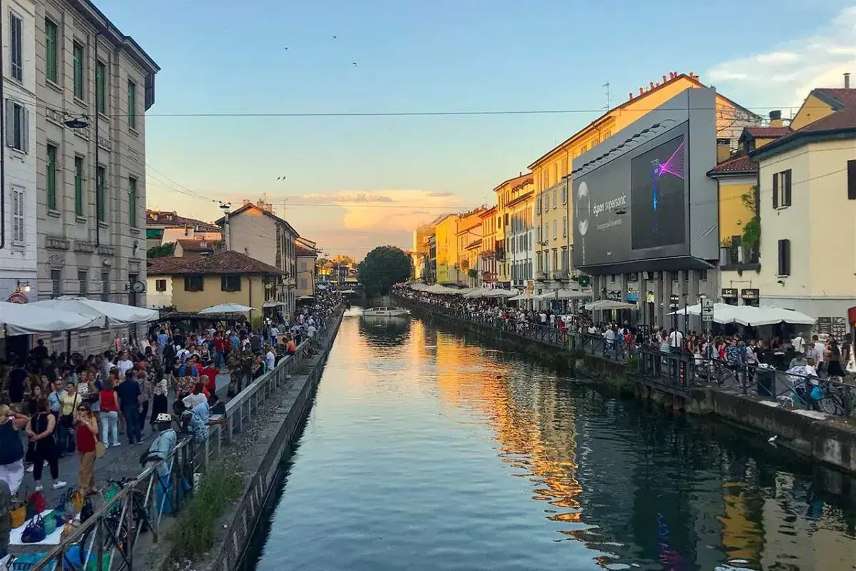 Tętniące życiem Navigli w Mediolanie. Ludzie spacerują wzdłuż kanału, ciesząc się wieczornym słońcem i atmosferą.