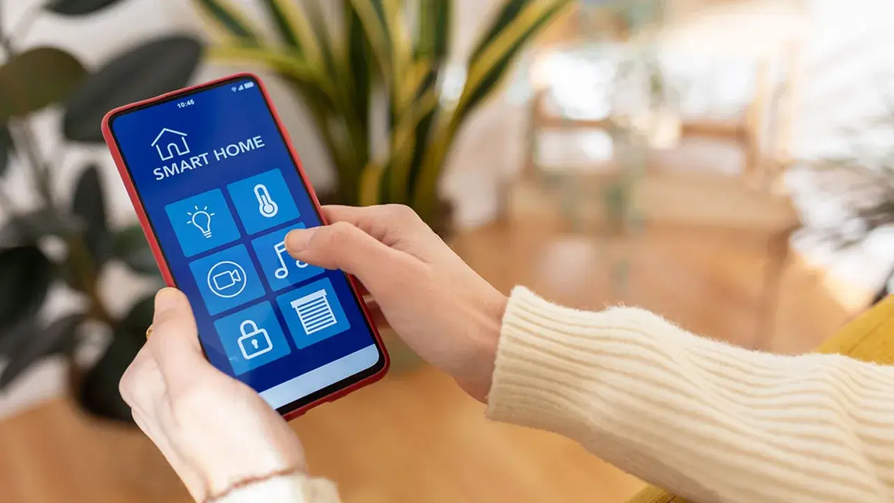 Mano usando un smartphone para controlar productos inteligentes de hogar: luces, temperatura, cámara, música y persianas.