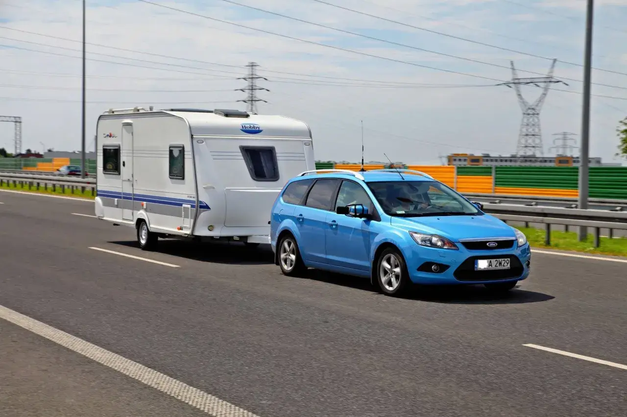 Niebieski Ford Focus z przyczepą kempingową Hobby na drodze. Zestaw mieści się w limitach maksymalna długość pojazdu z przyczepą kat b.