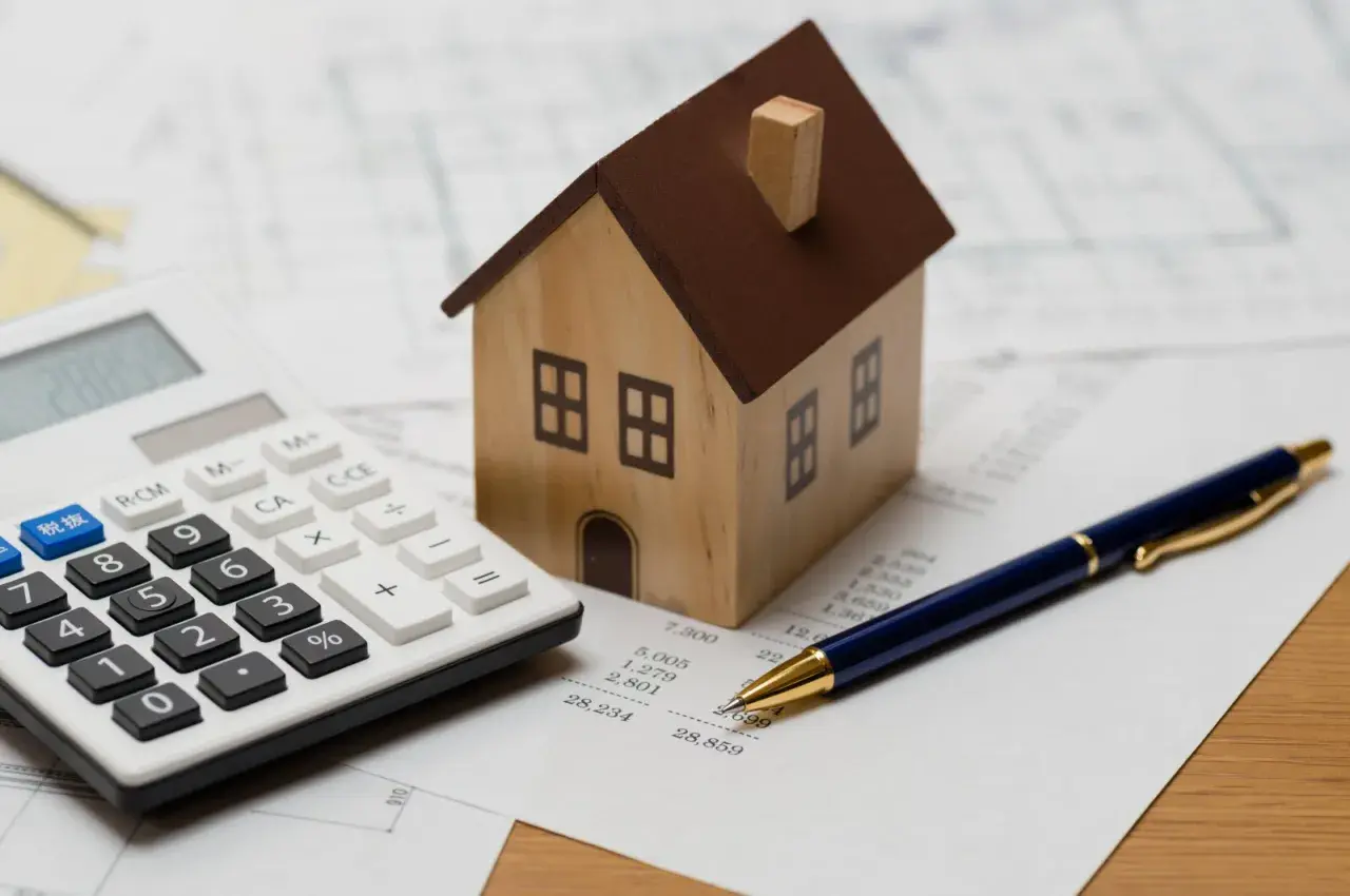Maquette de maison, calculatrice et stylo sur des documents financiers. Idéal pour illustrer un avis Camif Habitat sur l'investissement immobilier.