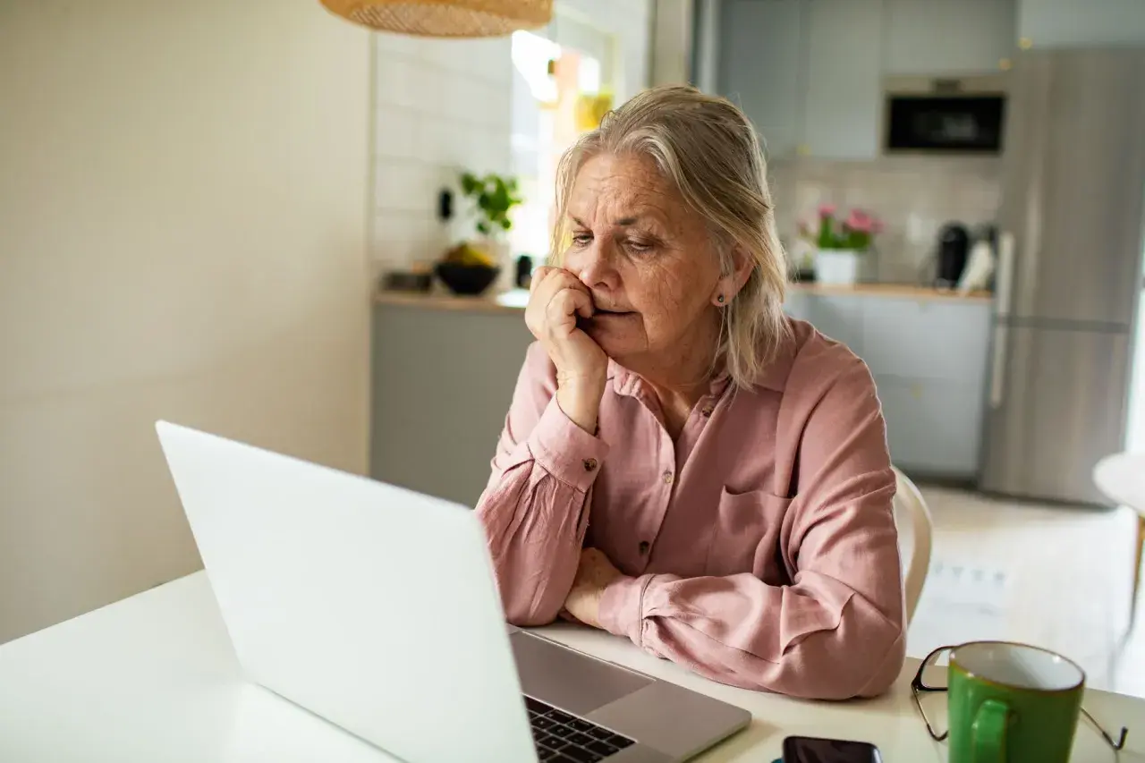 Femme âgée réfléchissant devant son ordinateur, cherchant des solutions pour savoir que faut il faire pour ne pas payer une maison de retraite.