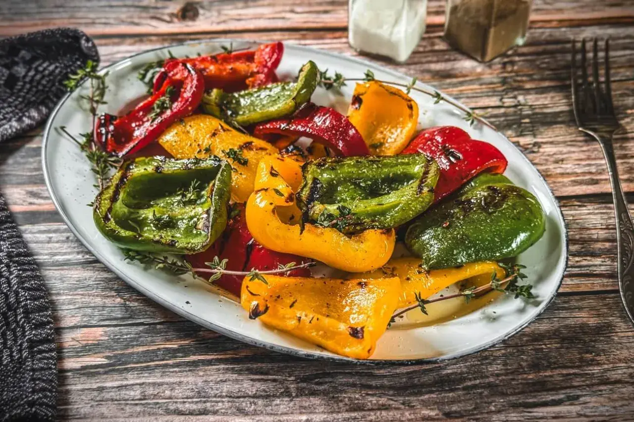Bunte, gegrillte Paprika, mit Kräutern verfeinert, auf einem Teller angerichtet. Ein Genuss für Augen und Gaumen.
