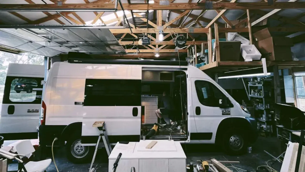 Aménagement d'un camion en cours dans un garage. Un homme travaille à l'intérieur, entouré d'outils et de matériaux.