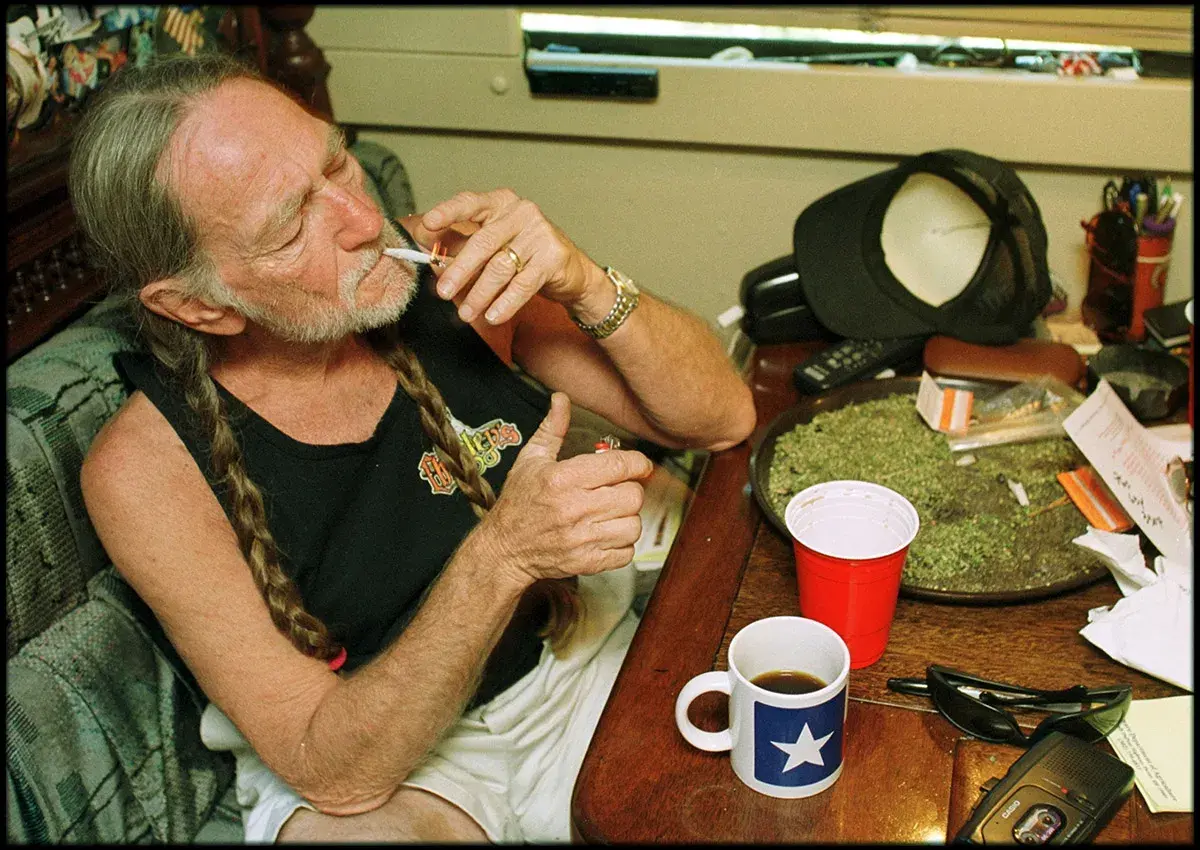 Willie Nelson, icona delle migliori canzoni country americane, accende una sigaretta con una tazza di caffè accanto.