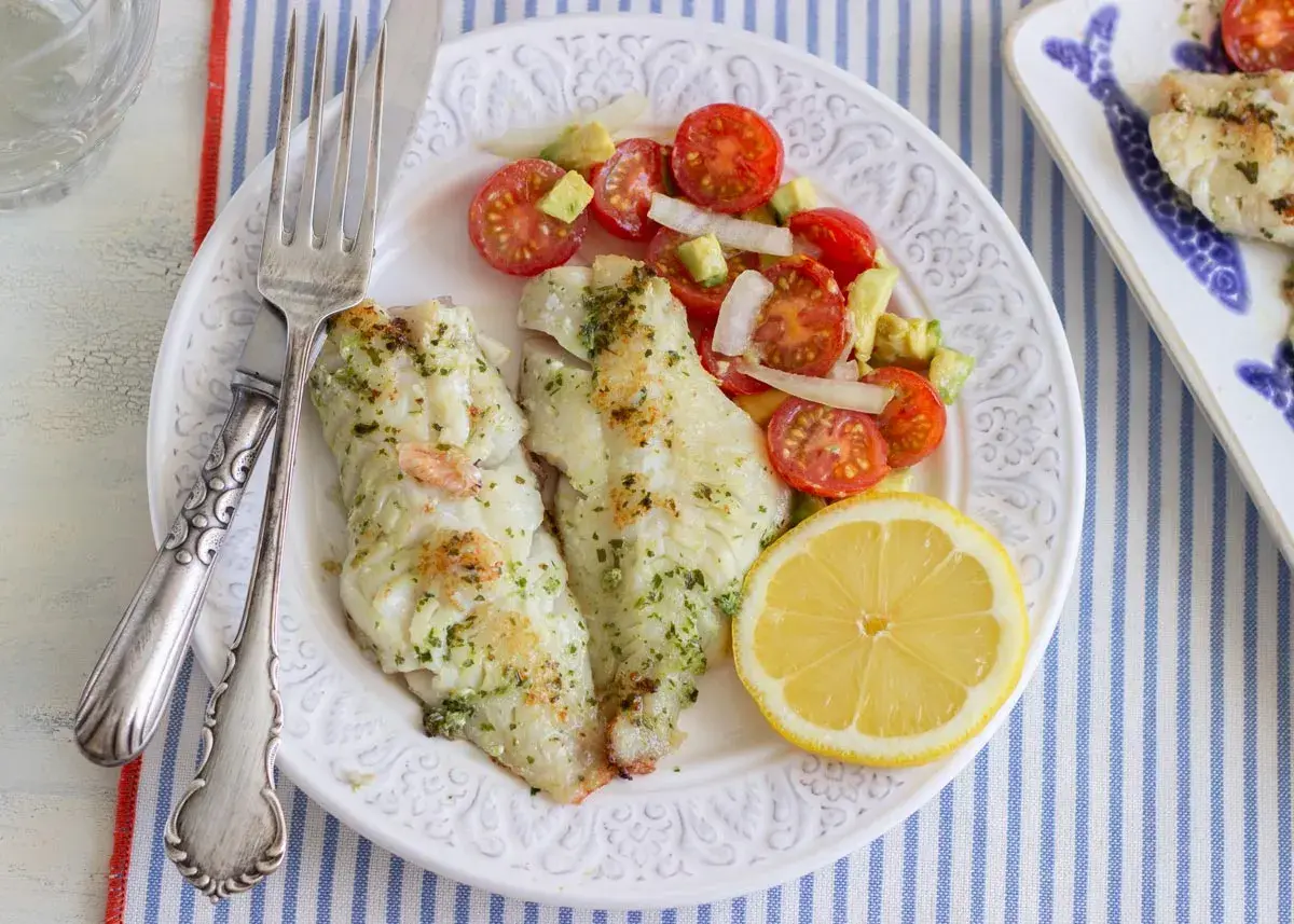 Deliciosa gallineta a la plancha con ensalada de tomate y aguacate, acompañada de un gajo de limón.