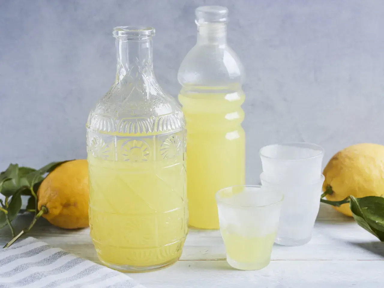 Ein Glas mit dem original italienischen Limoncello Rezept, daneben eine Karaffe, Flasche und Zitronen.