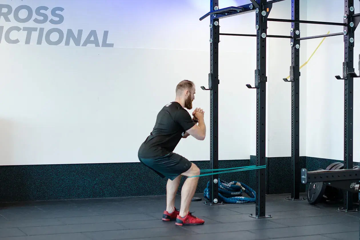 Mężczyzna wykonuje ćwiczenie spanish squat z gumą oporową wokół ud, w siłowni.