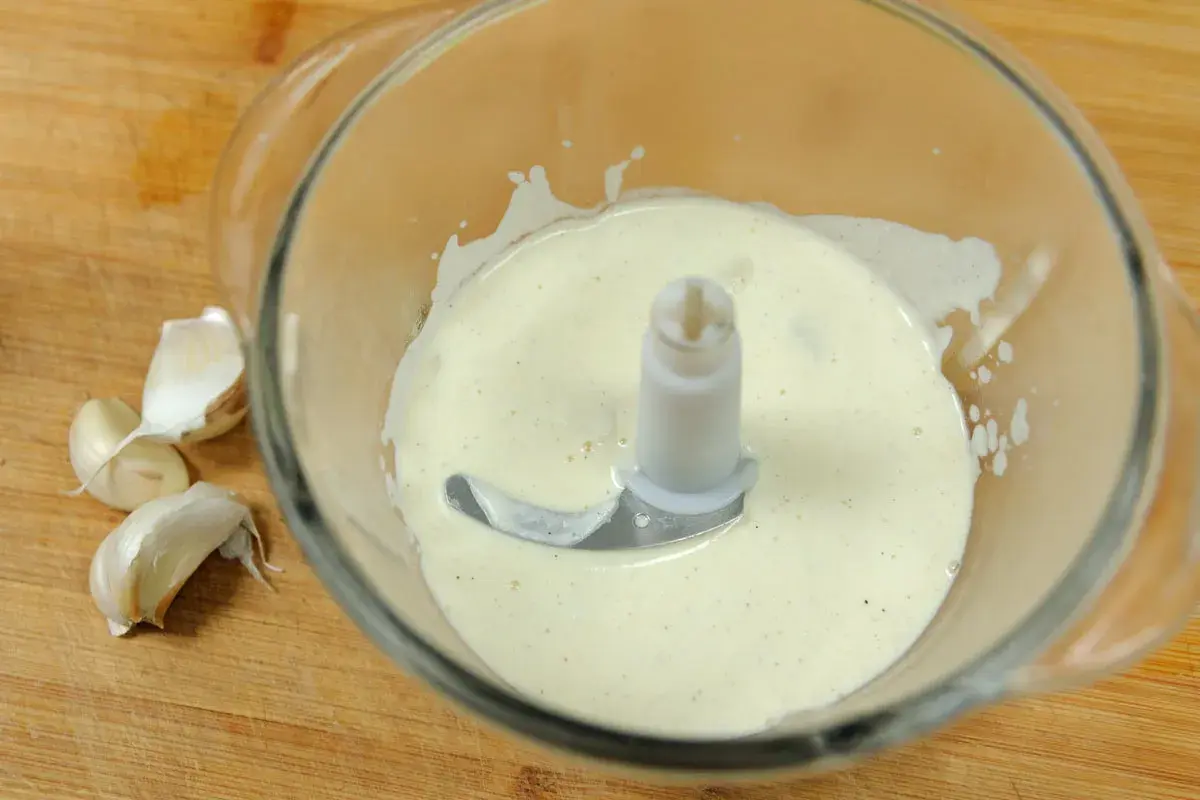 Crème d'ail onctueuse dans un mixeur, prête à être dégustée. Quelques gousses d'ail frais à côté.