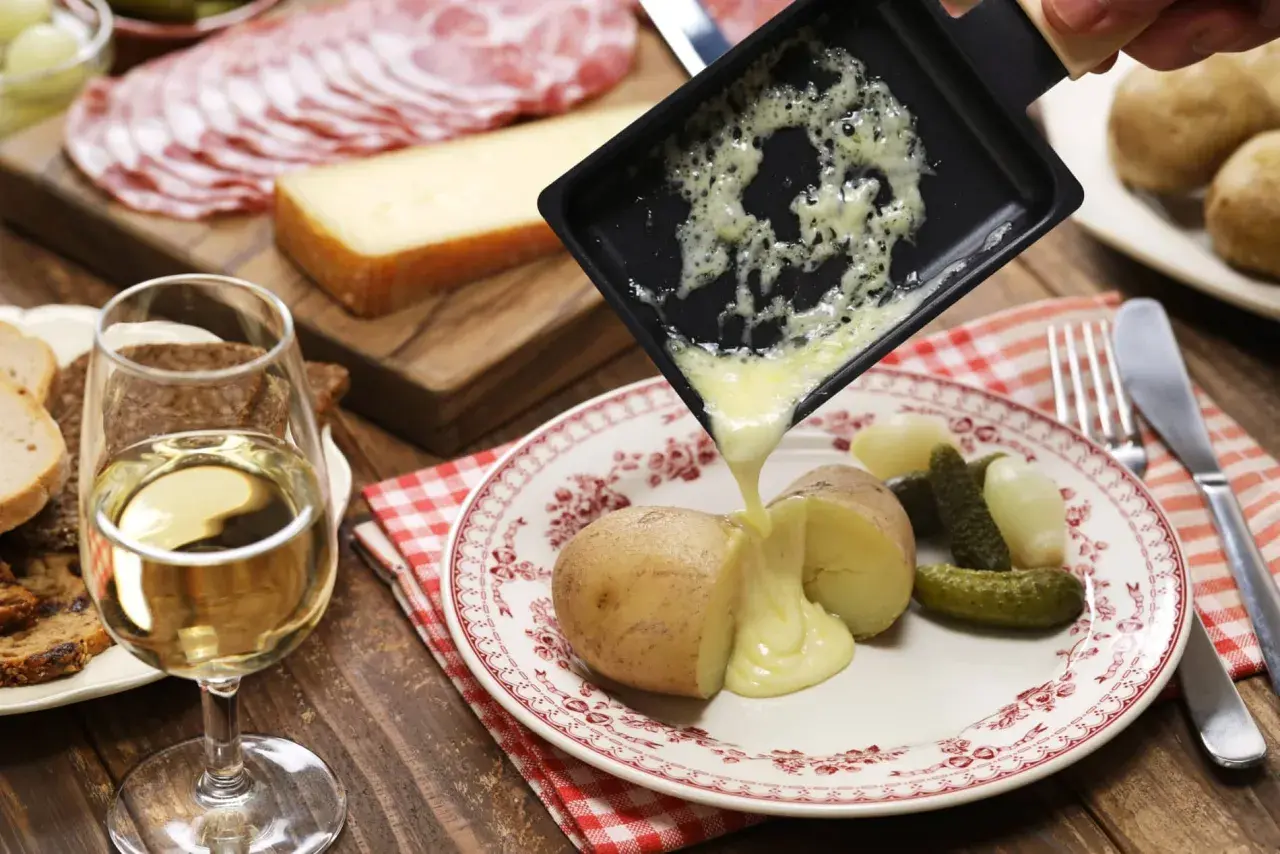 Un accord plat vin parfait : raclette fondue sur pommes de terre, cornichons, charcuterie et pain, avec un verre de vin blanc.