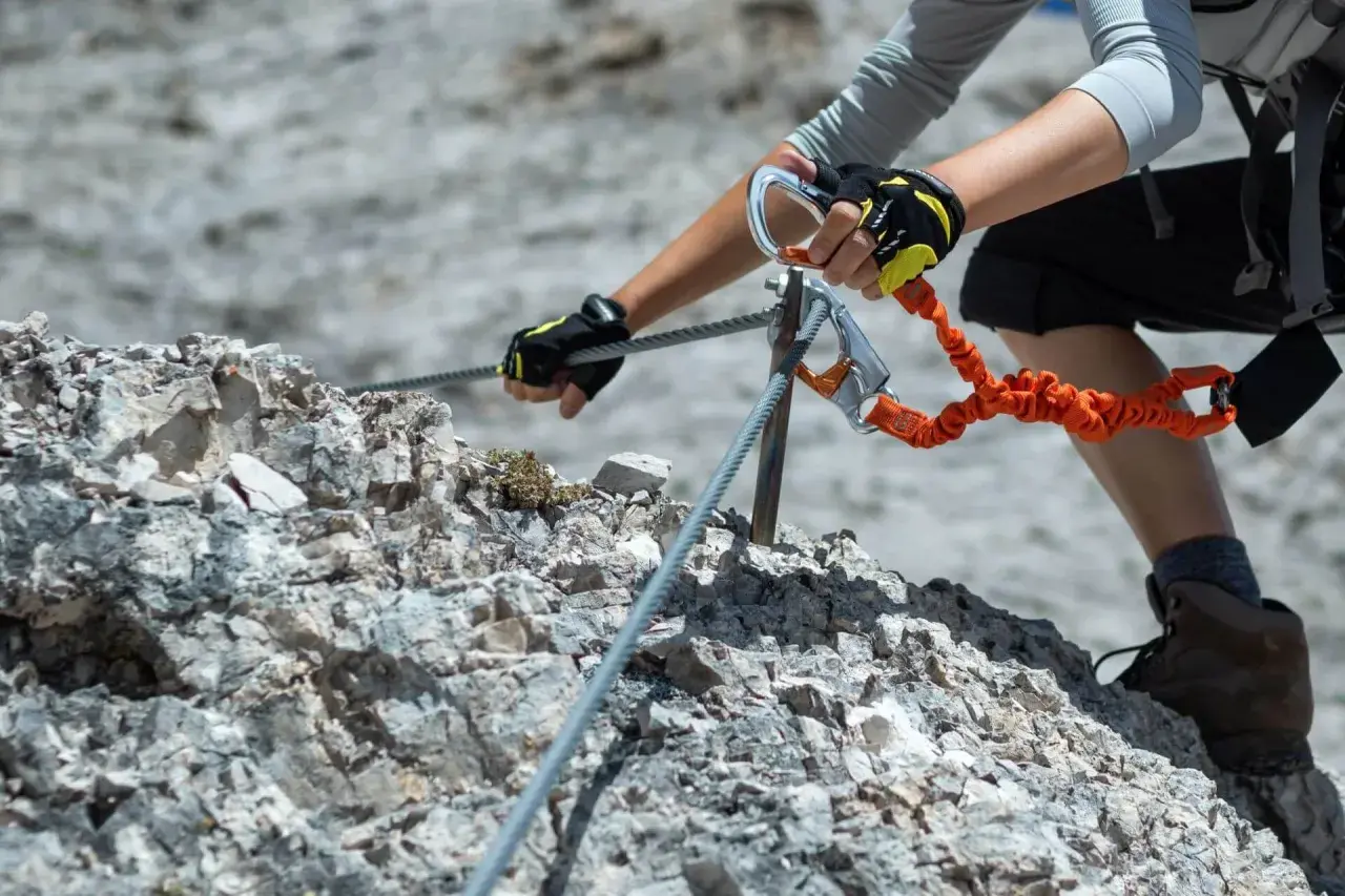 Ręce w rękawiczkach z karabinkami zabezpieczają się na stalowej linie podczas wspinaczki. To przygoda na via ferrata Słowacja.