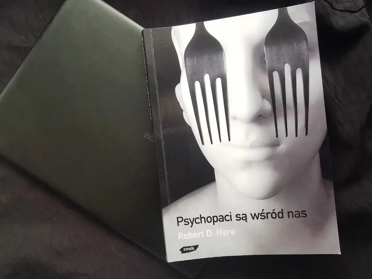 Okładka książki "Psychopaci są wśród nas" z widelcami zamiast oczu na twarzy.