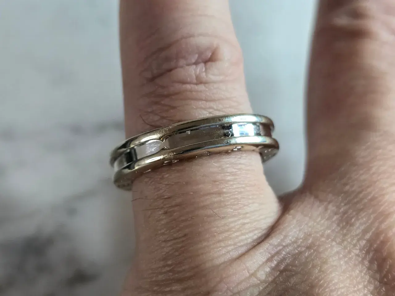 Anillo Bulgari de oro blanco y detalles pulidos, adornando un dedo con su diseño elegante y atemporal.