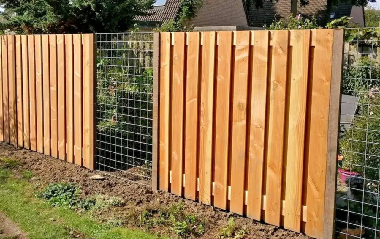 Clôture en bois reconstitué, avec des planches verticales et une section grillagée. Un chien est visible derrière le grillage.