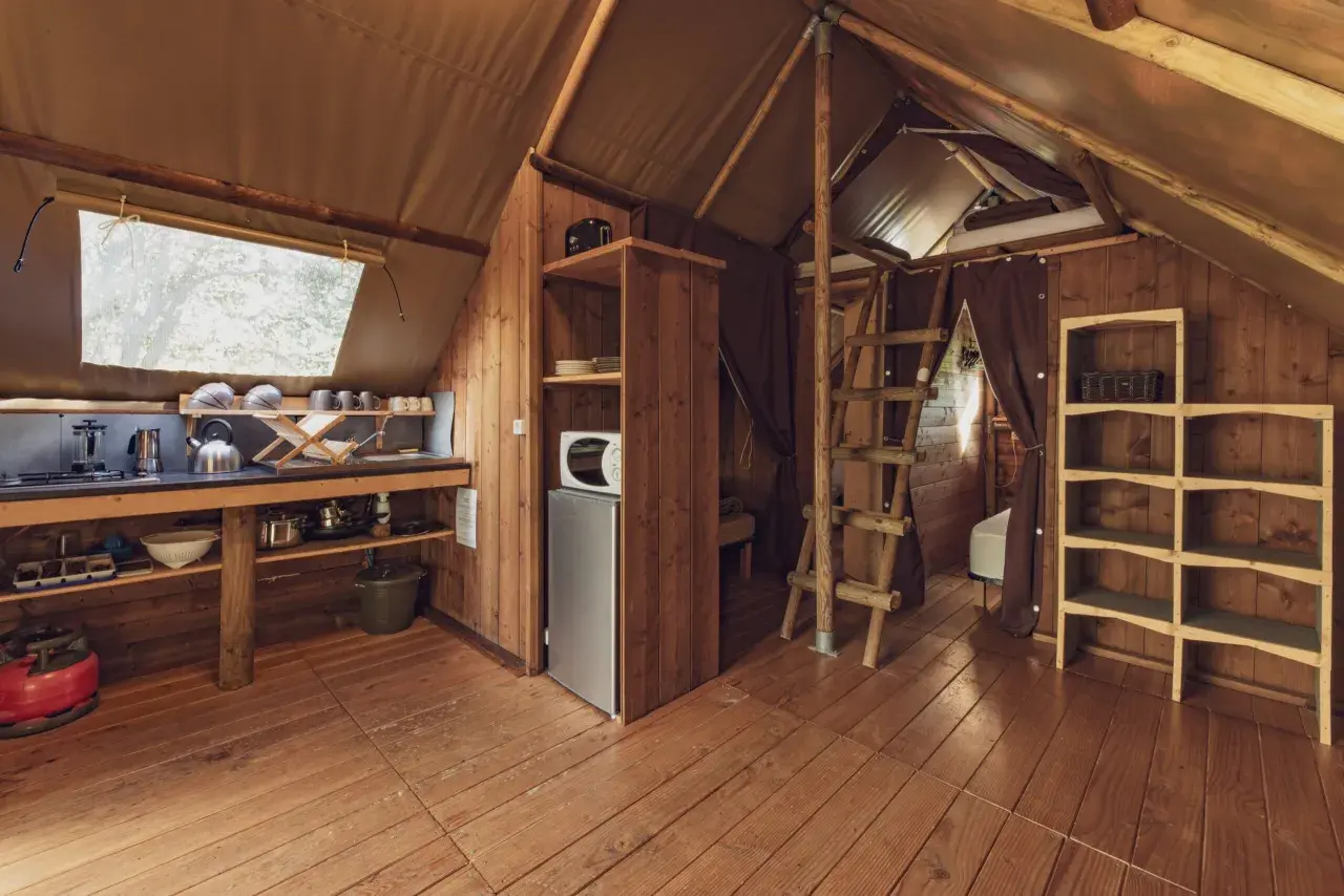 Intérieur d'une cabane en bois avec coin cuisine, réfrigérateur, étagères et échelle menant à un lit. Un havre de paix en Haute-Loire.