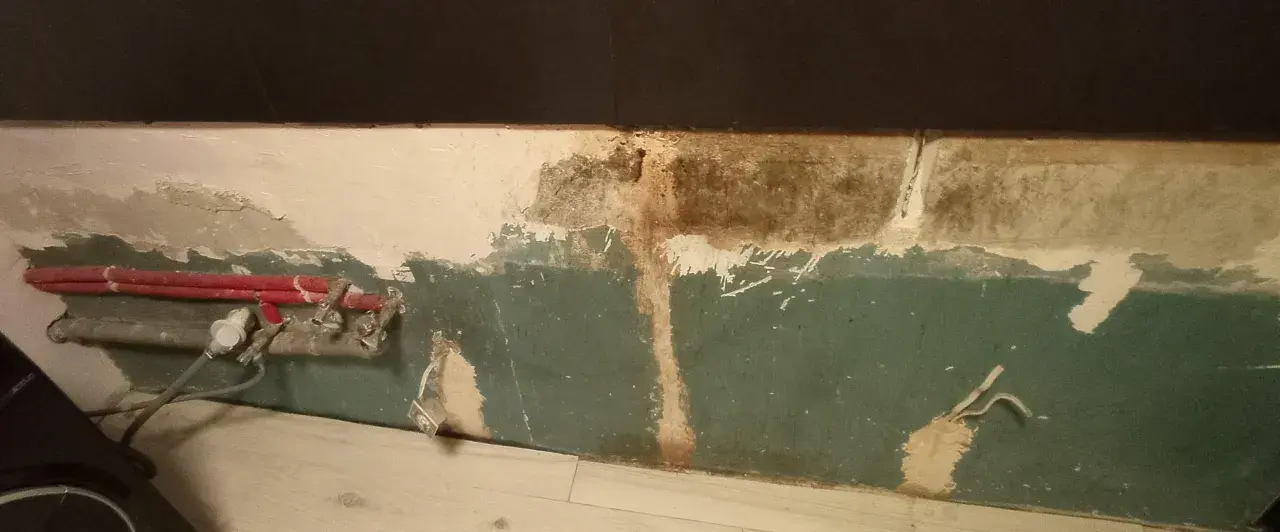 Preparazione per carteggiare muro per imbiancare: tubi rossi e impianto a vista, intonaco scrostato e macchie.