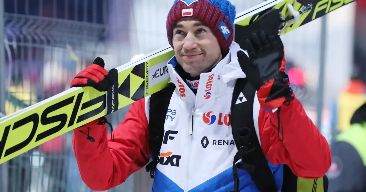 Uśmiechnięty Andrzej Stoch Jr. z nartami na ramieniu, gotowy do skoku.