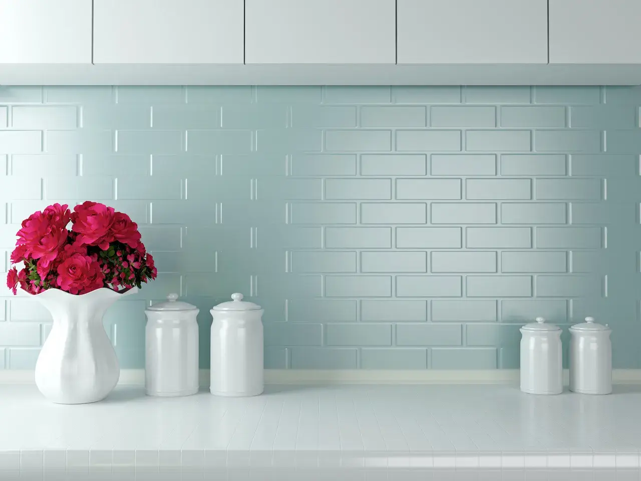 Un mazzo di rose rosse in un vaso bianco su un piano di lavoro, con barattoli bianchi e uno sfondo di piastrelle azzurre. Ottime opinioni per dipingere piastrelle cucina.