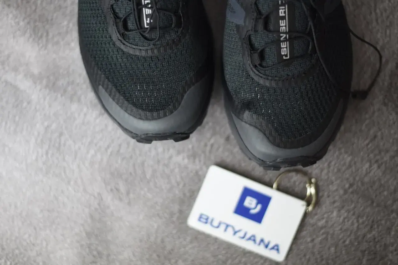 Czarne buty Salomon, model Sense Ride, z metką "BUTYJANA". Salomon to znana firma produkująca odzież i obuwie sportowe.