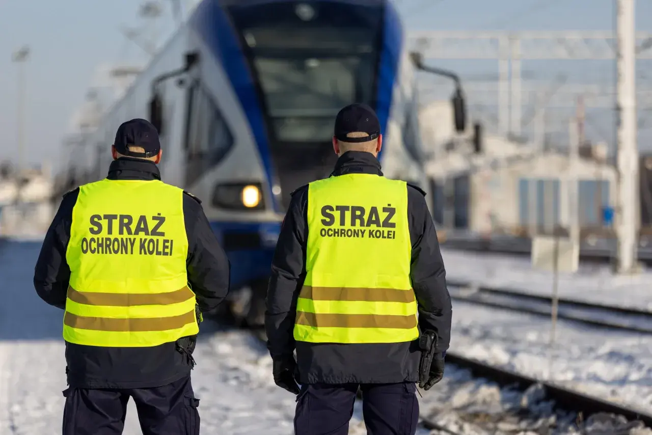 Dwóch funkcjonariuszy Straży Ochrony Kolei w kamizelkach odblaskowych stoi przed pociągiem. Działają na mocy ustawy o straży ochrony kolei, zapewniając bezpieczeństwo.