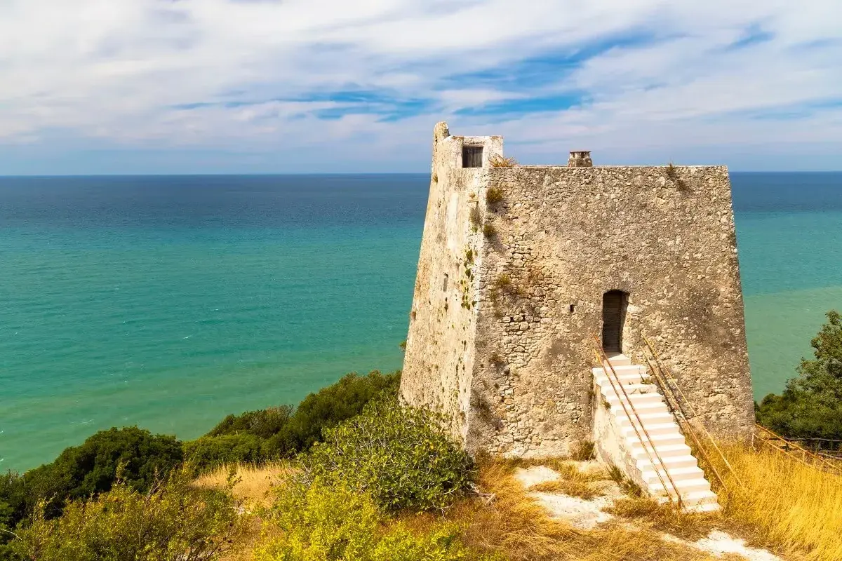 Torre costiera in pietra con mare turchese sullo sfondo, un luogo suggestivo tra i tanti posti da visitare in Puglia.