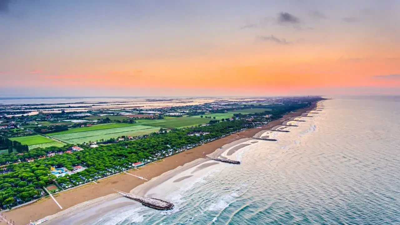 Alba sul mare veneto, con la spiaggia dorata, pineta rigogliosa e lagune all'orizzonte.
