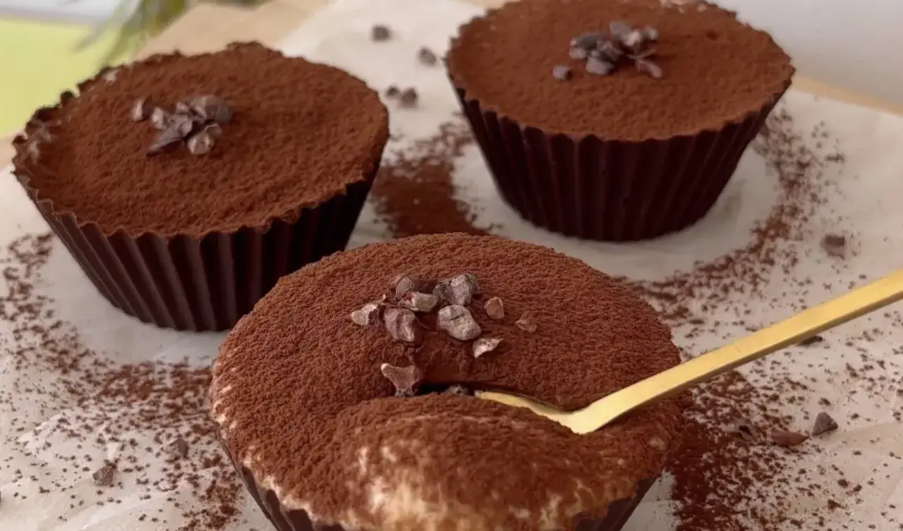 Delicioso postre con ricota, cubierto de cacao y trocitos de chocolate. Una cuchara dorada se hunde en uno de ellos.