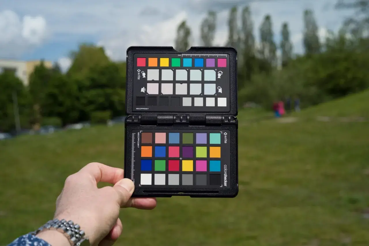 Dłoń trzyma otwartą kartę X-Rite ColorChecker, aby ustawić prawidłową temperaturę barwową w plenerze.