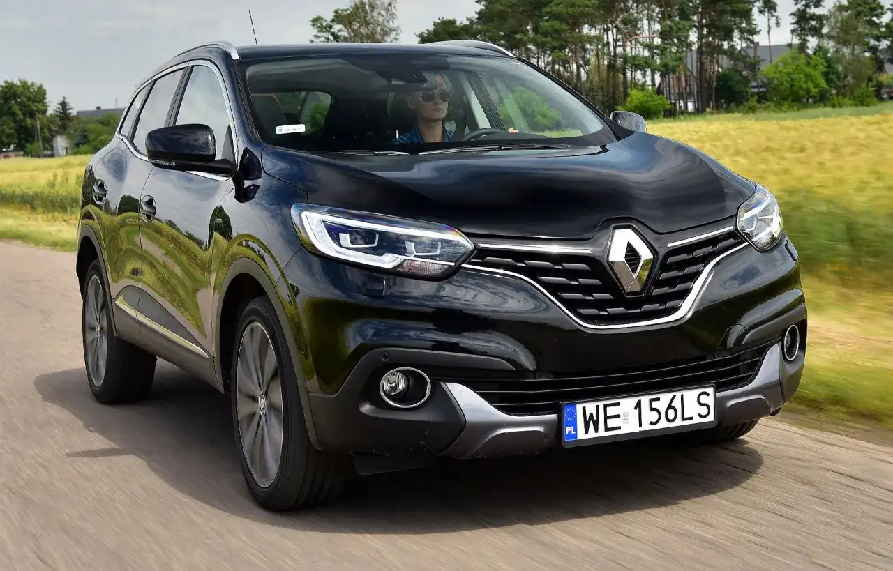Czarny Renault Kadjar w ruchu. Kierowca w okularach przeciwsłonecznych. Wiele pozytywnych renault kadjar opinie potwierdza jego walory.