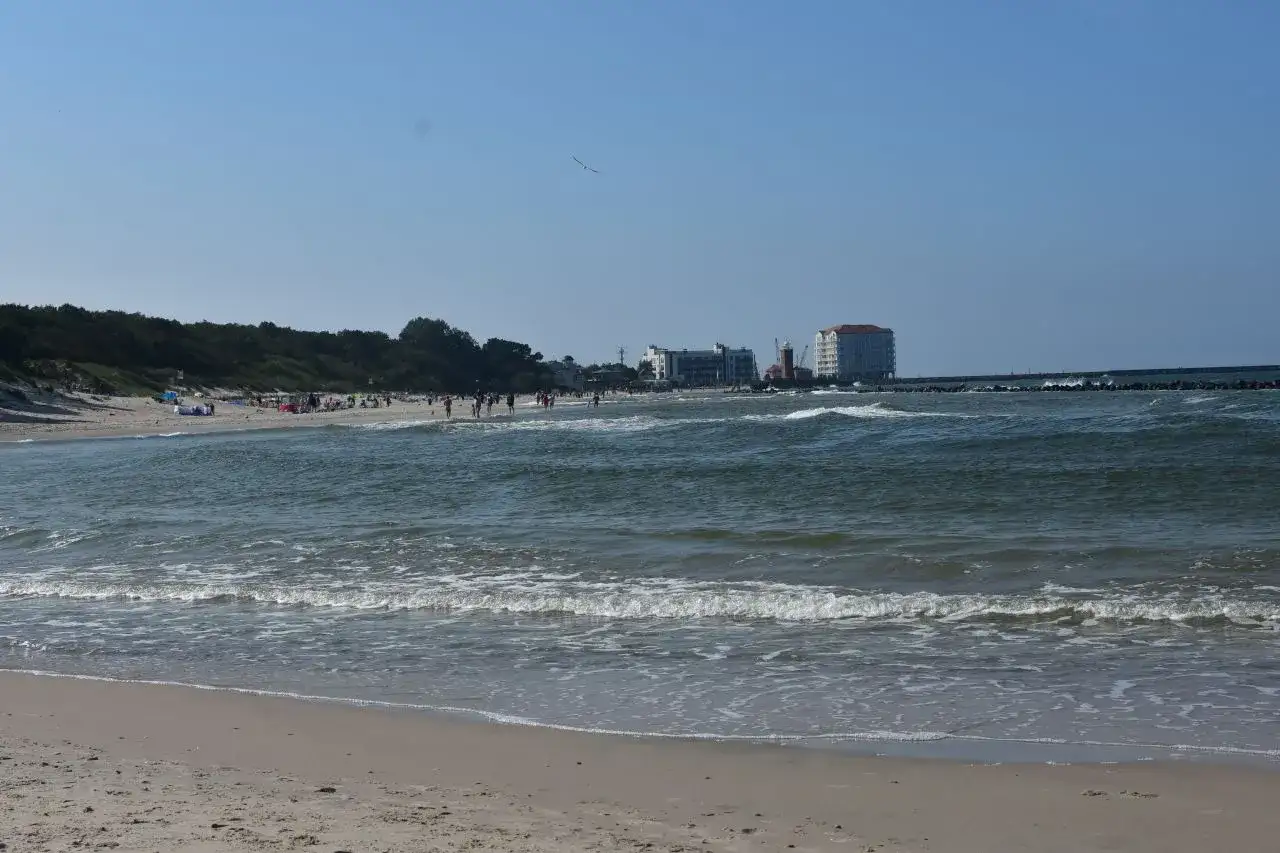 Słoneczny dzień nad Bałtykiem, plaża pełna ludzi, a w oddali widać miasto u ujścia Wieprzy.