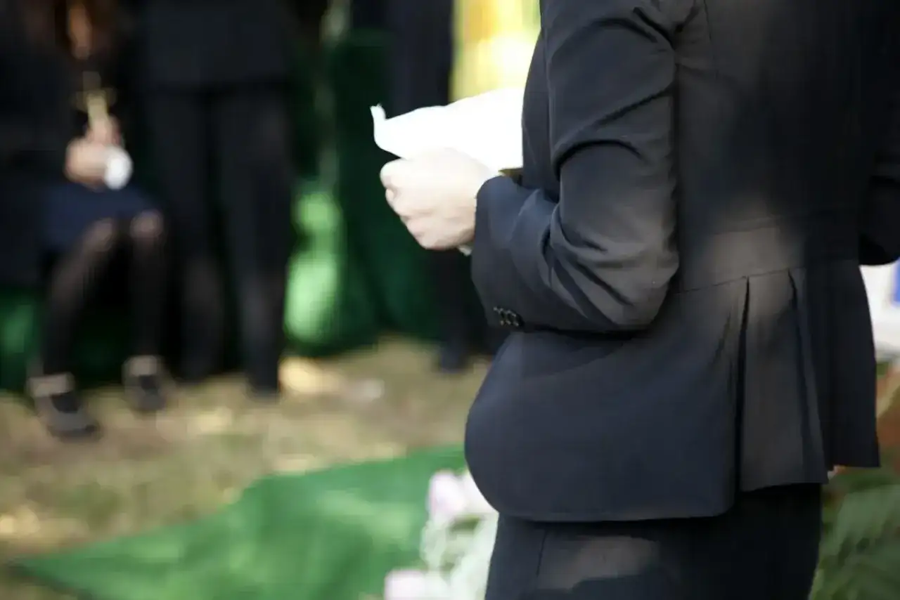 Smutne wspomnienie o zmarłej osobie. Kobieta w czerni trzyma kartkę, być może przemówienie pożegnalne.