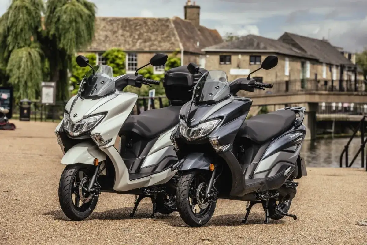 Dwa skutery Suzuki Burgman 125, jeden biały, drugi grafitowy, stoją obok siebie. Sprawdź suzuki burgman 125 cena!