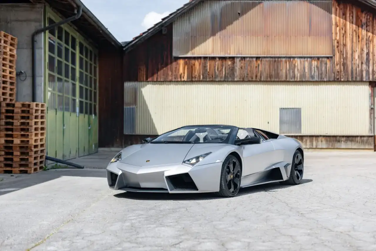 Srebrny, otwarty Lamborghini Reventon stoi przed rustykalnym budynkiem.
