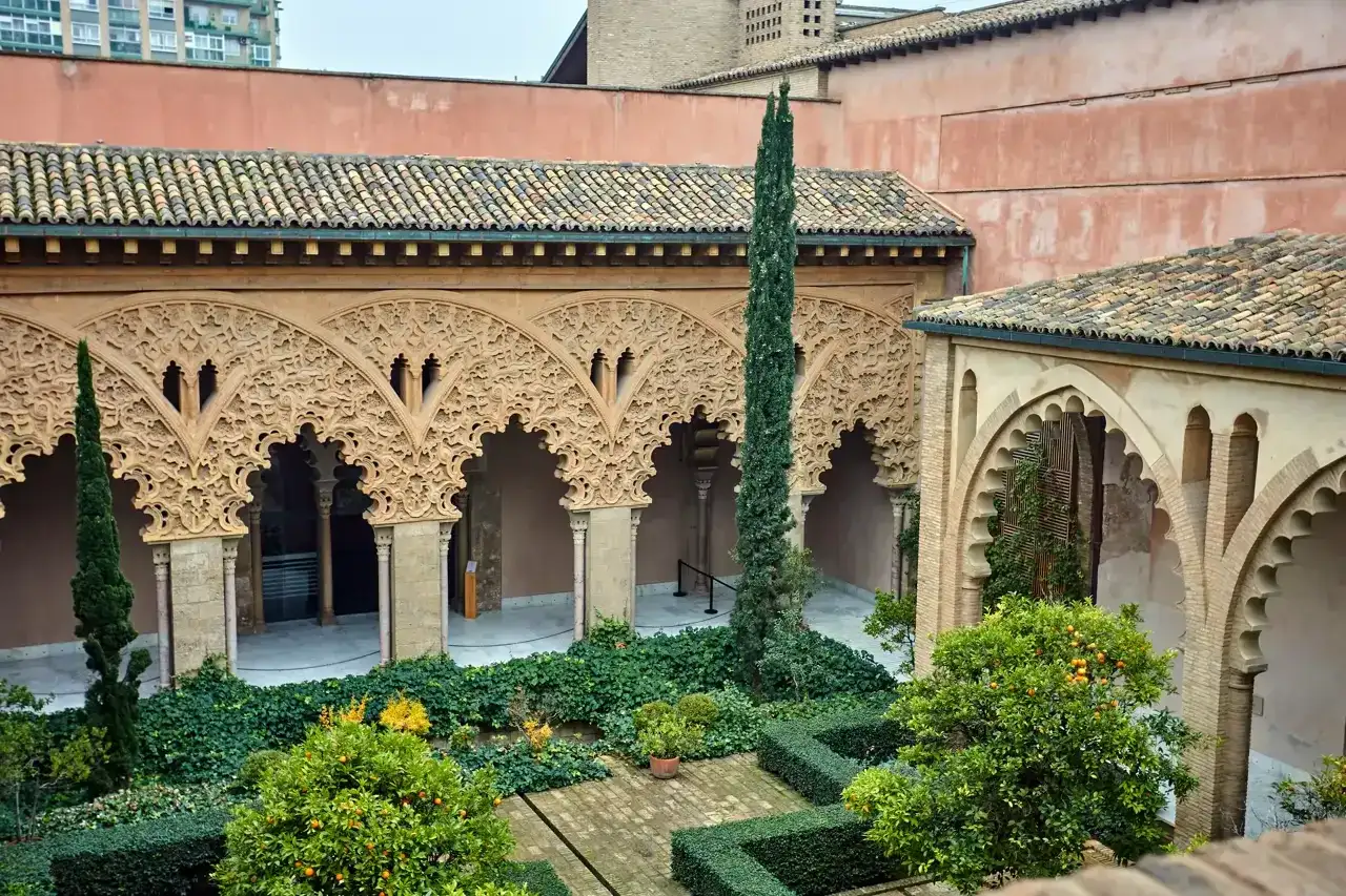 Patio de la casa de los Morlanes con arcos de yesería intrincada, vegetación exuberante y naranjos cargados de frutos.