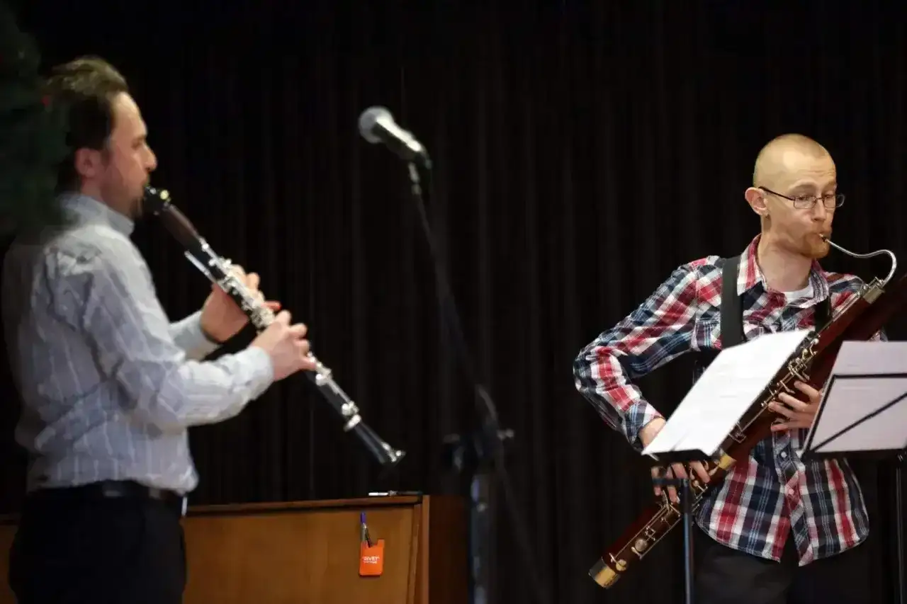 Dwóch muzyków gra na instrumentach dętych. Jeden na klarnecie, drugi na fagocie. Przed nimi stoją nuty na klarnet znane piosenki.